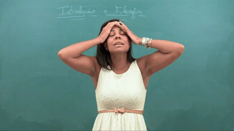 A frustrated teacher standing in front of a blackboard, pressing her hands to her forehead.