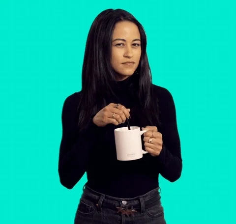 A young woman holding a cup of coffee and looking suspicious as she stirs coffee.