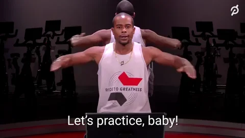 Peloton instructor wearing a white tank top, clapping on a bike. Caption reads 