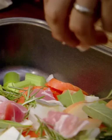 somebody is cooking vegetables in a frying pan, adding bacon.