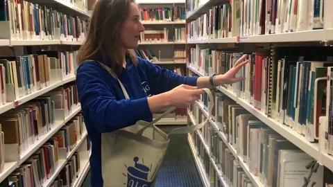 A woman grabbing books and putting them into a bag in the library.
