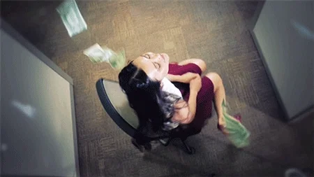 A woman spins in an office chair as money rains down on her from the ceiling.