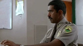 A police officer character from the movie Super Troopers, typing at a computer, instructing it to 