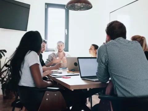 A group of colleagues at a table in a meeting room discussing work tasks.