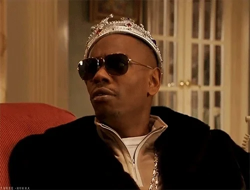 Dave Chappelle wearing a jeweled crown and hugging cash.