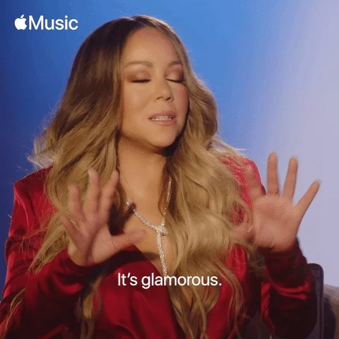 Mariah Carey wears a fancy outfit  moving her head and hands confidently with overlaid text that reads 'it's glamorous.'