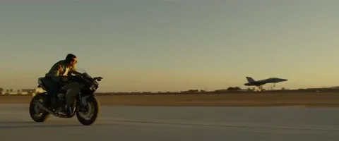 Tom Cruise in the film Top Gun: Maverick riding alongside a fighter plane into the sunset on his motorbike.