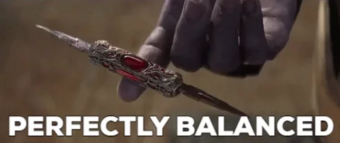 Thanos holds gemstone on his finger while overlaid text reads 'perfectly balanced.'
