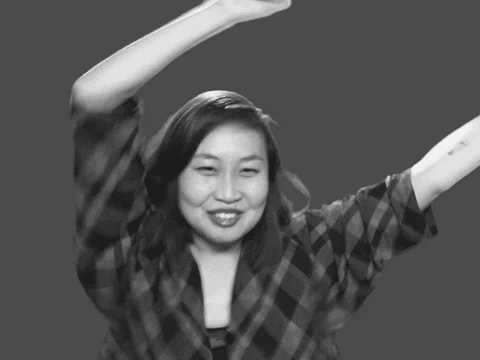 A woman wearing a checked T-shirt jumps up and down and waves her arms while saying, 'Do it!'