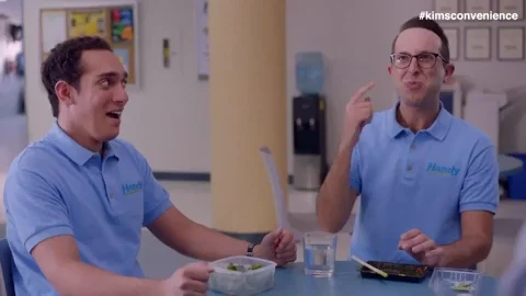 Two coworkers sit at a table. One excitedly points to his head and says, “Brain burn!”