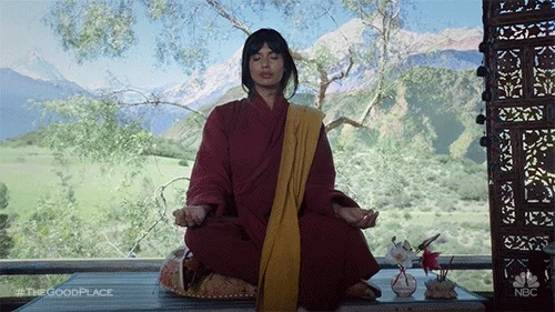 Tahani from The Good lPace meditates in front of a serene mountain landscape. 