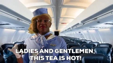 A man is dressed as a female flight attendant. He is holding a teacup and says, 