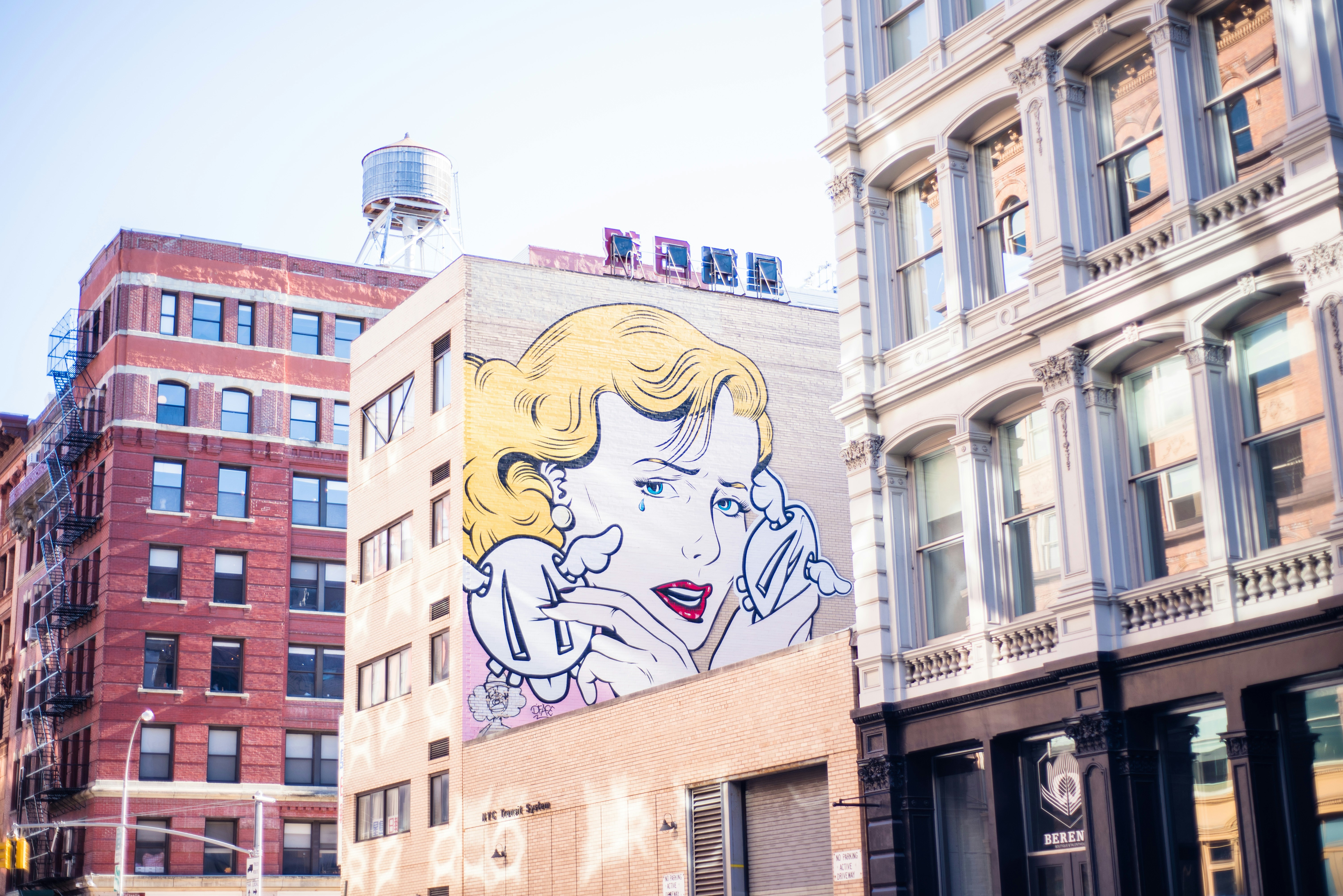 On the side of a building, a large mural shows a crying figure with blond hair who is holding two white items with wings. 