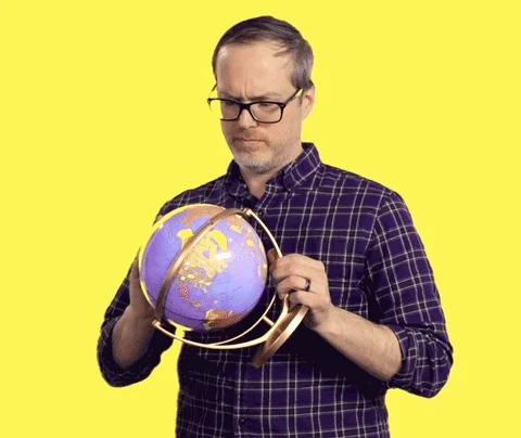 A man spinning globe, randomly pointing to a country, and nodding and smiling.