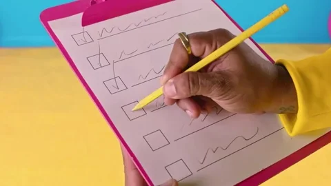 A pink clipboard with a checklist is in the center. A person's hand holding a pencil checks off the 4th item on the list. 