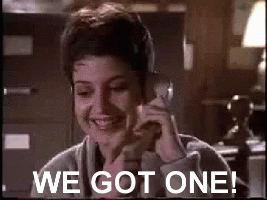 A laughing woman hanging up a phone and yelling, "We got one!".