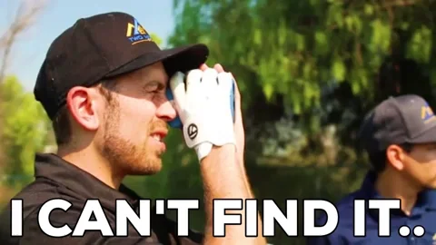 Two golfers looking for a ball. One golfer looks through binoculars and says, 