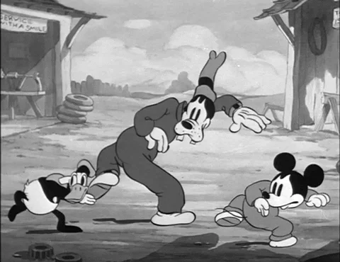 Mickey Mouse, Goofy and Donald Duck in an old black and white animation creeping slowly through a village.