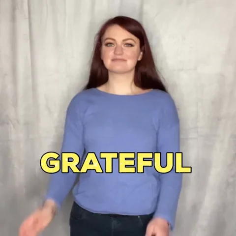 A woman smiles warmly with her hands pressed together in a gesture of gratitude, saying "grateful."