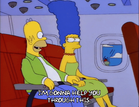 Homer and Marge Simpson on an airplane. Homer is holding Marge's hand and saying, 'I'm gonna help you through this.'
