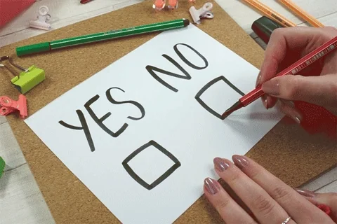 A sheet of paper on a desk shows the words “yes” and “no” with checkboxes below each. A person marks an X in the “no” box.