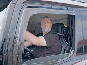 A joyful trucker making a playful arm gesture sitting in his truck.
