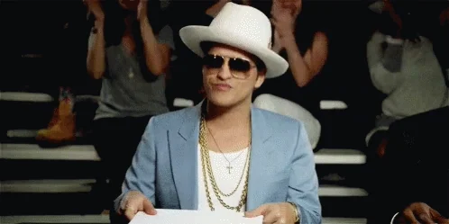 Bruno Mars judging a competition. He holds up a board with 
