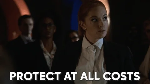 Serious woman in a room of people, saying: "Protect at all costs"