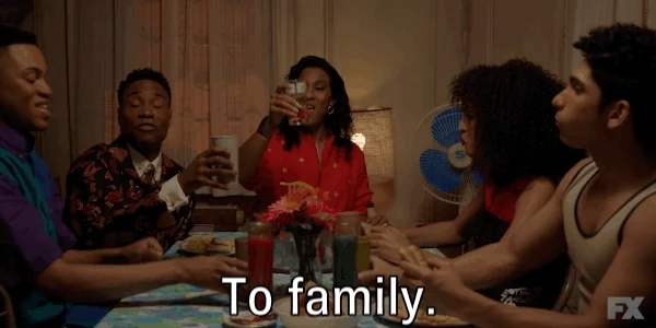 Group of people sitting at a table, raising their glasses in a toast, and stating 'To family.'