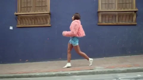 A girl wearing a pink fur coat and shorts are walking with a confidence.