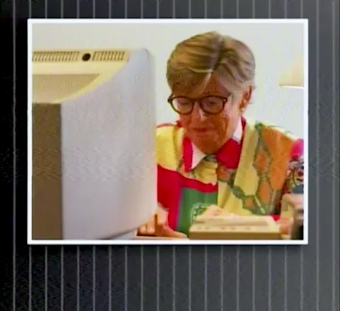 An elderly woman sitting at a desktop computer. She is typing while saying, 'I'm hacking!'