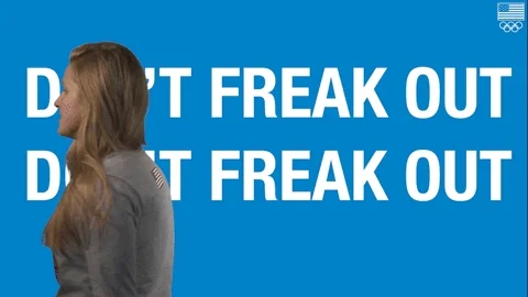 A girl paces back and forth in front of a large sign that says "Don't Freak Out", with a tense posture and downward gaze.