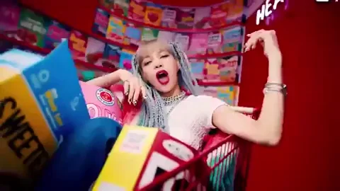 A pop singer rides down a grocery store aisle in a shopping cart filled with cereal boxes.