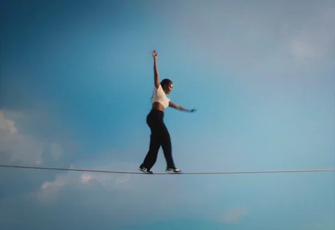 A woman struggling to balance on a tightrope.