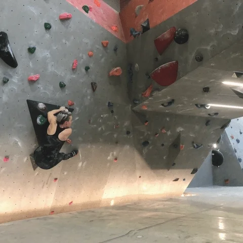 A person at a bouldering gym, jumping from one hold to another