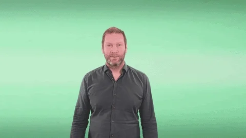 A man in front of a green screen. He clicks his fingers and the background changes to Caribbean bungalows on water. 