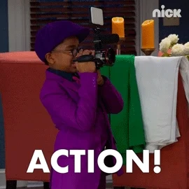 A young boy in a purple suite holding and looking through a film camera and yelling, 