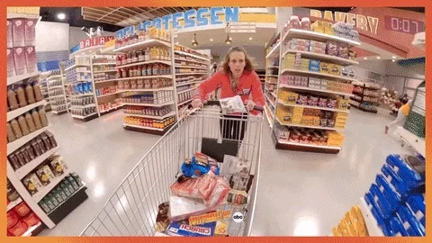 Lady frantically runs through food aisle at grocery store. She throws food into her cart.