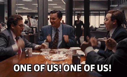 Wolf of Wall Street characters pounding an office table, chanting 'One of us! One of us!'