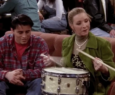 Phoebe from the TV show 'Friends' playing a drum while sat on a sofa