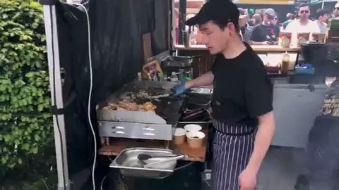 young man wearing apron cooking at a street food grill giving a thumbs up