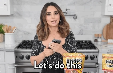 Young woman with shoulder-length wavy hair wearing a black bodysuit and black pants in a kitchen  saying 'Let's do this.'