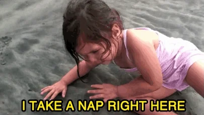 A baby laying down on beach while crying, saying, "I take a nap right here."
