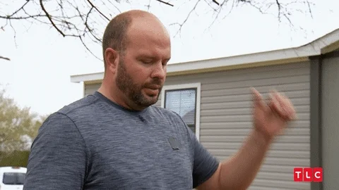 A man standing outdoors in deep thought while scratching his head.