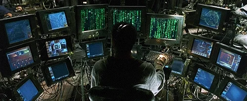 A person is sitting in front of 17 monitors typing on a keyboard with their right hand. 
