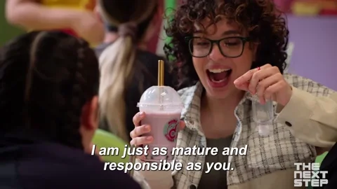 A curly haired caucasian girl holding a strawberry milkshake. She says, 'I'm just as mature and responsible as you.'