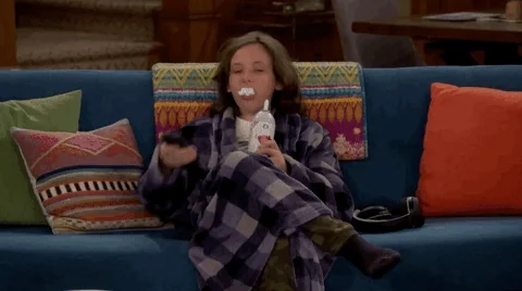 A girl turns on the TV and lounges on the couch. 
