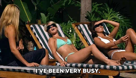 A woman lounges on a beach chair, sunglasses on, jokingly saying, “I’ve been busy.”