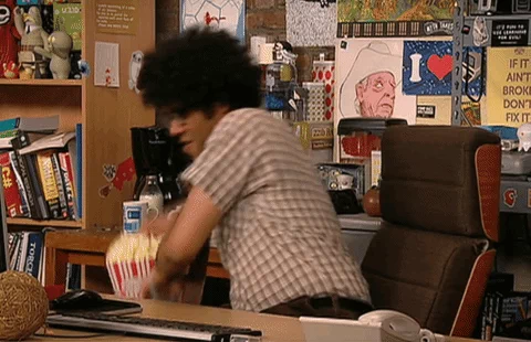 Moss from the I.T. Crowd puts a large popcorn and drink on his desk, and says 