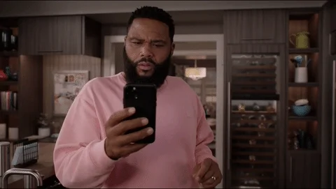 Anthony Anderson looks at his phone. He has a confused expression on his face.